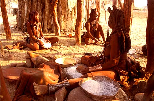 Young Himba women grinding maize in evening sun